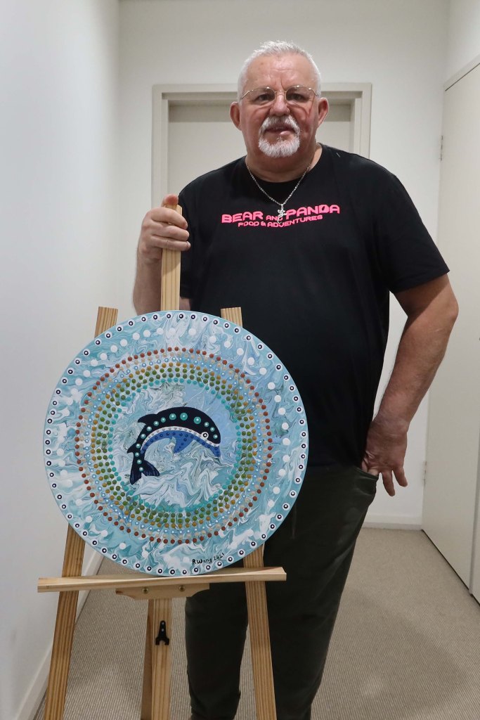 Robb Wang beside a circular dolphin artwork