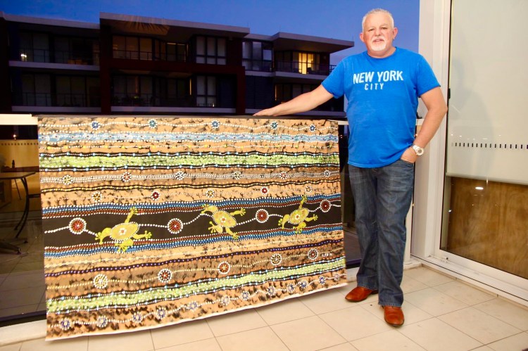 Robb Wang standing beside a large painting with kangaroo figures